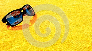 Sunglasses closeup summer background. Beach pool equipment with travel sunglasses on yellow holiday towel. Outdoor relax