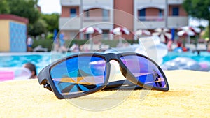 Sunglasses closeup summer background. Beach pool equipment with travel sunglasses on yellow holiday towel. Outdoor relax