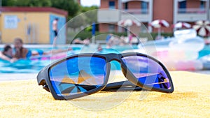 Sunglasses closeup summer background. Beach pool equipment with travel sunglasses on yellow holiday towel. Outdoor relax