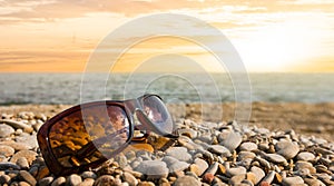 Sunglasses lie on a stony sea beach at the sunset