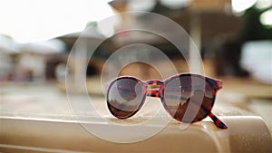 Sunglasses lying on the chaise-longue. Unrecognizable people, sandy beach, chasers and the sea are on a blurred