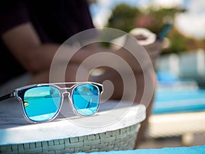 Sunglasses, Men`s sitting in a swimming pool background. Summer holiday traveling concept design banner with copyspace