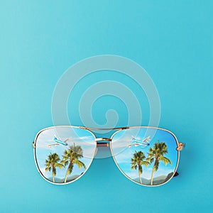 Sunglasses with palm trees, a plane and mountains reflected in them. Concept on the theme of vacation and travel with copy space