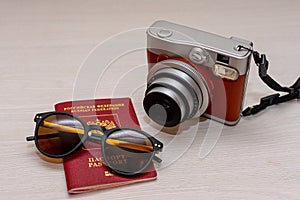 Sunglasses with the passport of a citizen of the Russian Federation and an instant photo camera on a white wooden background