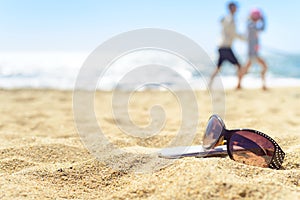 Sunglasses and phone on the beach with people on background