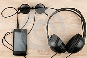 Sunglasses, phone and headphones lying on a wooden table, with space for your text.