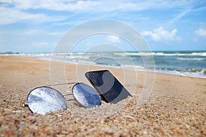 Sunglasses and phone are placed on beach and reflections of bright sky