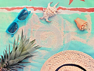 sunglasses, pineapple, straw hat and shells on a beach towel