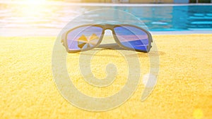 Sunglasses pool summer background. Beach pool equipment with travel sunglasses on yellow holiday towel. Sun glasses near