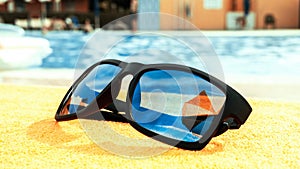Sunglasses pool summer background. Beach pool equipment with travel sunglasses on yellow holiday towel. Sun glasses near