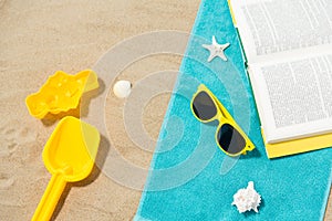 Sunglasses, sand toys and book on beach towel