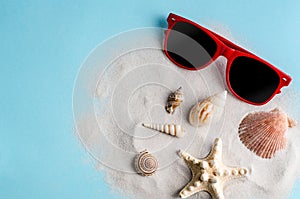 Sunglasses and sea shells on clean sand on a blue background