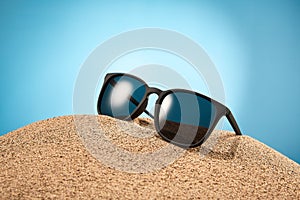 Sunglasses, shades with black frame, lenses in sand.