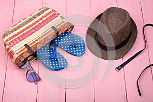 sunglasses, straw beach bag, sun hat, belt and flip flops on pink wooden table