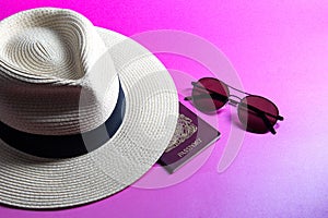 Sunglasses with Straw Panama Hat and Passport on a Pink Surface