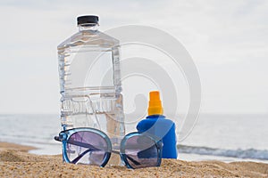 Sunglasses, Sunscreen and bottle of water on sand beach