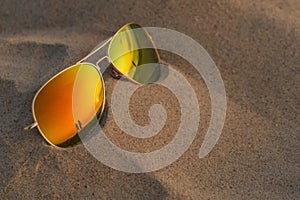 Sunglasses with sunset and couple reflection in sand at beach