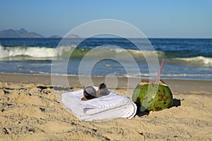 Sunglasses, towel and a fresh young coconut on the sandy beach with blurred Atlantic ocean in background