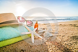 Sunglasses, towels, hat, sun block, shells and starfish on sandy