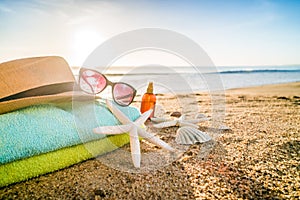 Sunglasses, towels, hat, sun block, shells and starfish on sandy