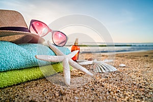 Sunglasses, towels, hat, sun block, shells and starfish on sandy