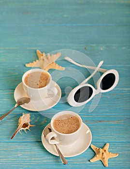Sunglasses and two white cups of coffee on a wooden blue background.
