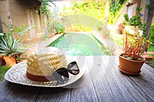 Sunglasses with vintage straw hat fasion on wooden table, Blur background for vintage resort hotel photo