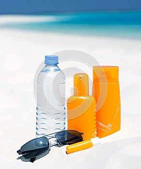 Sunglasses, water and sun protection cream on beac