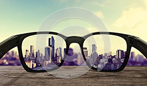 Sunglasses on wooden desk, focused on lens city view