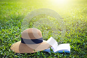 Sunhat and book lying on a lush green garden lawn under the hot rays of the sun