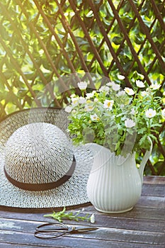 Sunhat with daisies in jug on table