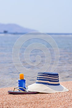 Sunhat, thongs and sunscreen on a beach