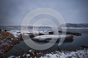 Sunken boats lie in a serene, snow draped bay as dusk falls on the quiet landscape