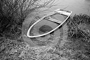 Sunken rowing boat lies on the shore of a frozen small lake