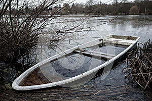 Sunken rowing boat lies on the shore of a frozen small lake
