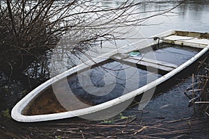 Sunken rowing boat lies on the shore of a frozen small lake