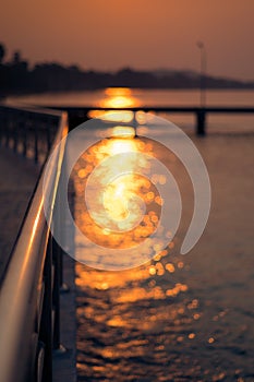 Sunlight with bokeh on water next to metal rail by the sea in Sattahip, Thailand.