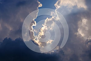 Sunlight breaking through white and dark clouds in the blue sky
