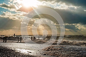 Sunlight breaks through the clouds and illuminating a pier and stormy beach