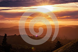 Sunlight bursting through the clouds and illuminating the hills and valleys of Santa Cruz mountains; clouds covering the sky and