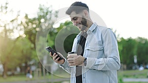 At sunlight handsome caucasian armenian young bearded man using phone stand on street at sunset. Mobile technology