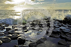 Sunlight highlighting waves crashing onto the hexagonal Basalt slabs of Giants Causeway