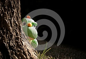 dinosaur doll peeking gesture behind tree trunk