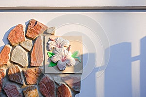 Sunlight and picket shadow on surface of decorative tile and rocks on white cement fence wall outside of vintage house