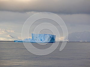 Sunlight picks out a lone blue iceberg before mountains in Antarctica