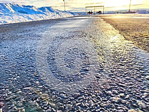Sunlight Reflecting on a Wet Asphalt Road. Sun peeks over a ice covered road, casting a glow on the textured surface