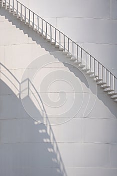 Sunlight and shadow on curved staircase surface of white storage fuel tank
