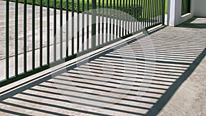 Sunlight and shadow on surface of automatic sliding metal fence gate in front of modern house