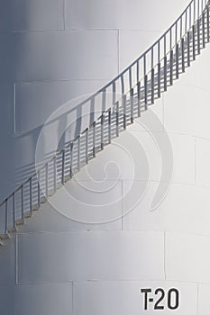 Sunlight and shadow on surface of curve spiral staircase on white oil storage fuel tank in vertical frame