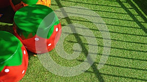 Sunlight and shadow on surface of decorative stucco garden seats in strawberry shape on artificial turf in front yard area